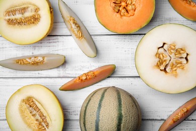Tasty colorful ripe melons on white wooden table, flat lay