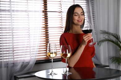 Photo of Beautiful young woman tasting luxury wine at table. Space for text