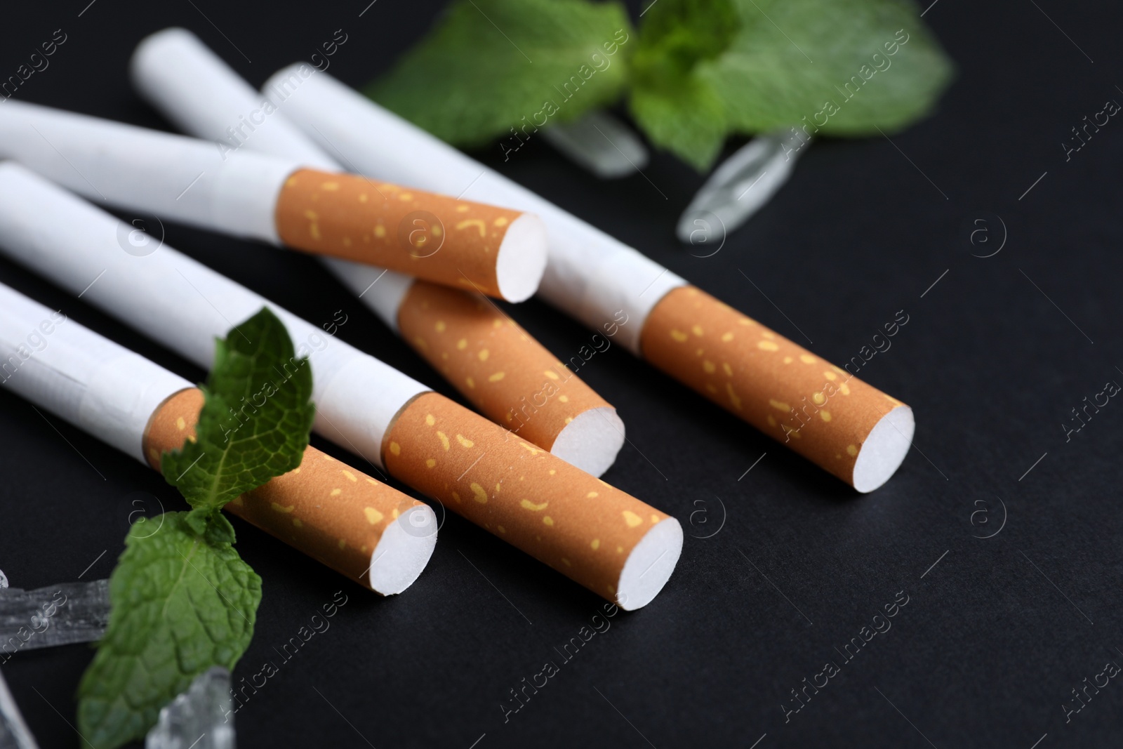 Photo of Cigarettes, menthol crystals and mint on black background, closeup