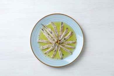 Tasty pickled anchovies with spices on white wooden table, top view