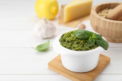 Delicious pesto sauce in bowl and ingredients on white wooden table. Space for text