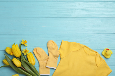 Flat lay composition with child's clothes and flowers on light blue wooden table. Space for text