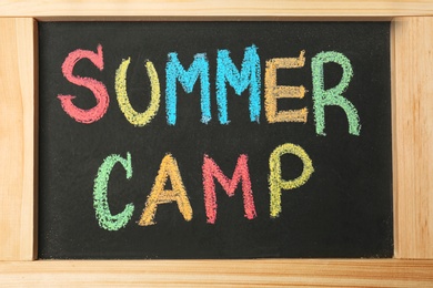 Photo of Little blackboard with inscription SUMMER CAMP chalked in different colors, closeup