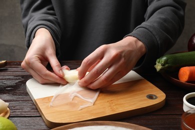 Making delicious spring rolls. Woman wrapping fresh cabbage into rice paper at wooden table, closeup