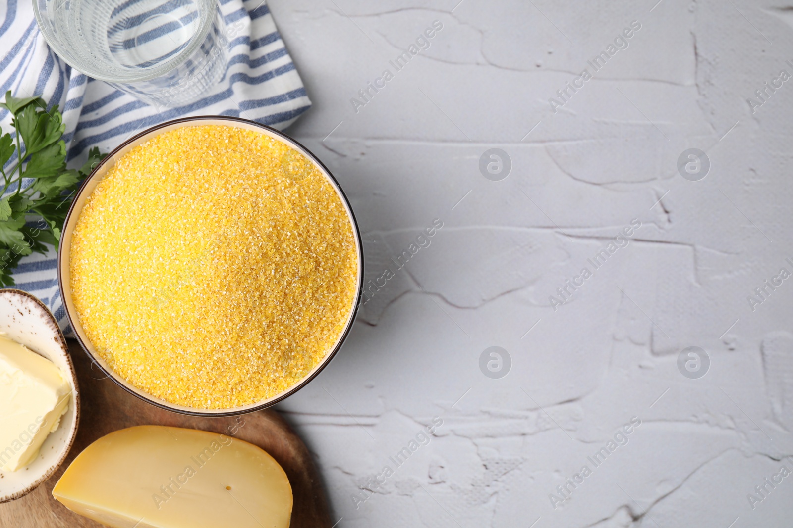 Photo of Raw cornmeal in bowl, cheese, parsley and butter on light textured table, top view. Space for text