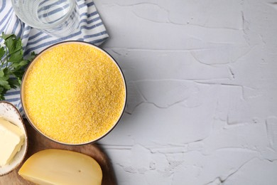 Photo of Raw cornmeal in bowl, cheese, parsley and butter on light textured table, top view. Space for text