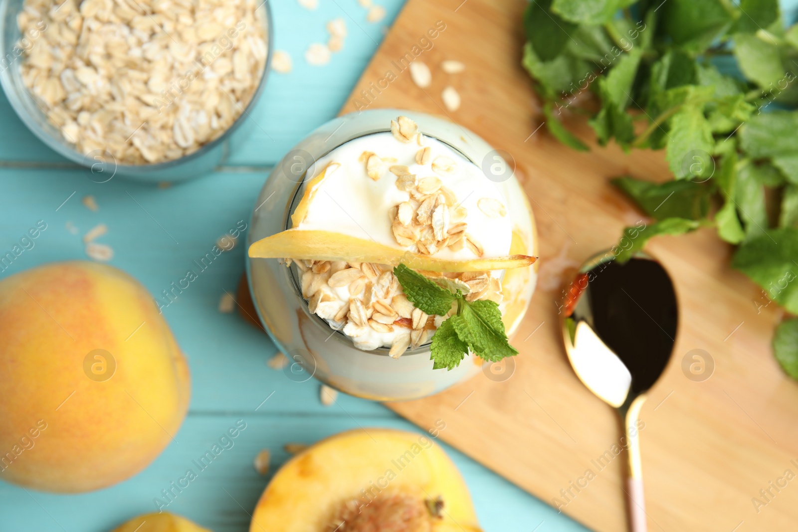 Photo of Tasty peach dessert with yogurt and granola served on light blue wooden table, flat lay