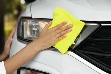 Photo of Woman cleaning car headlight with rag, closeup view