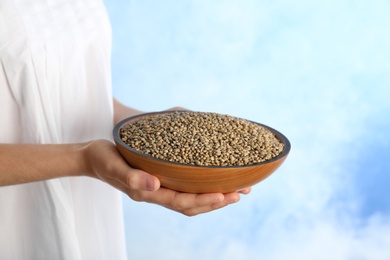 Photo of Woman holding bowl with hemp seeds on color background, closeup