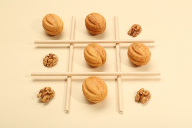Photo of Tic tac toe game made with walnuts and cookies on beige background