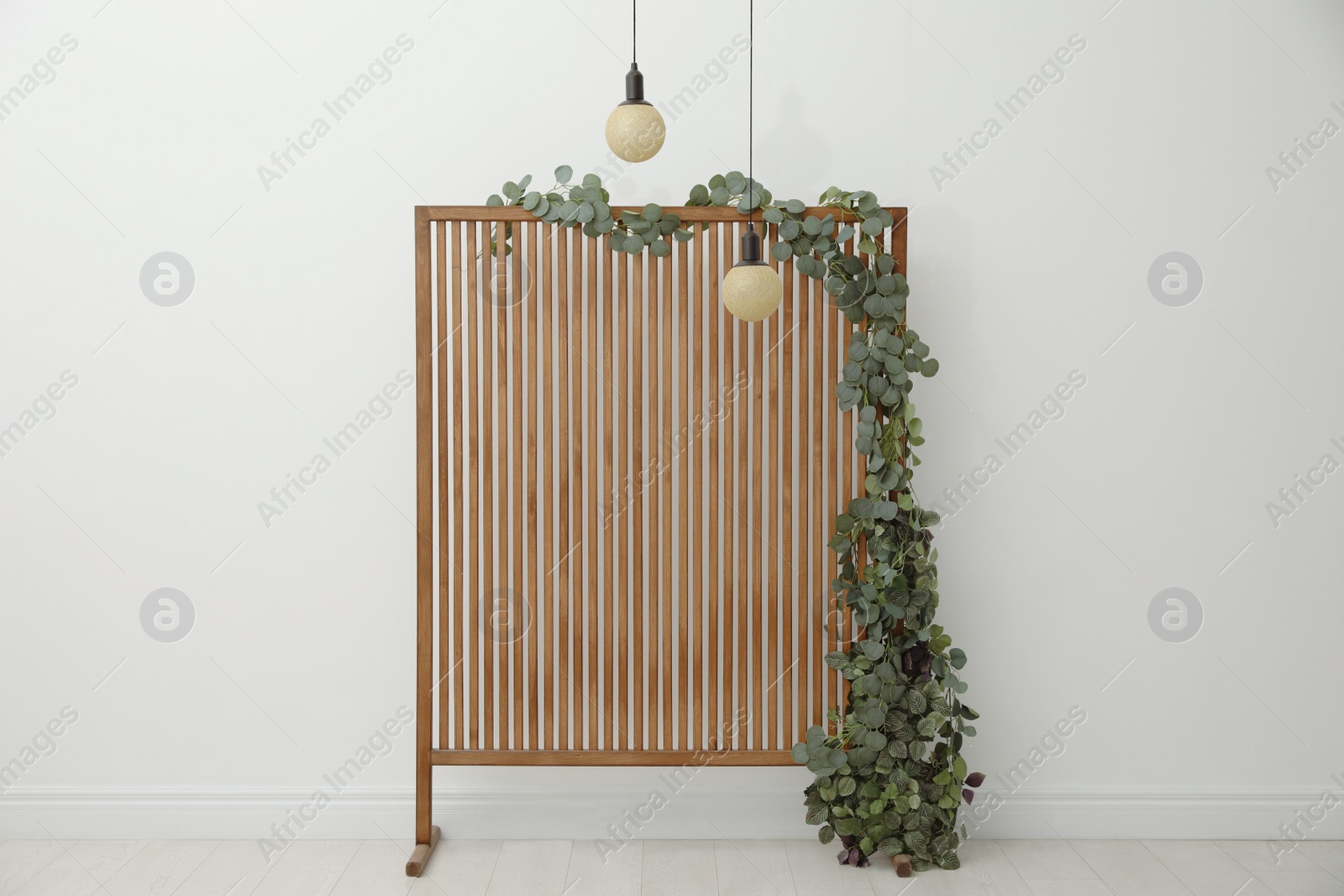 Photo of Stylish photo zone with wooden screen, floral decor and pendant lamps indoors