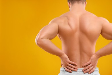 Photo of Man suffering from back pain on orange background, back view. Space for text