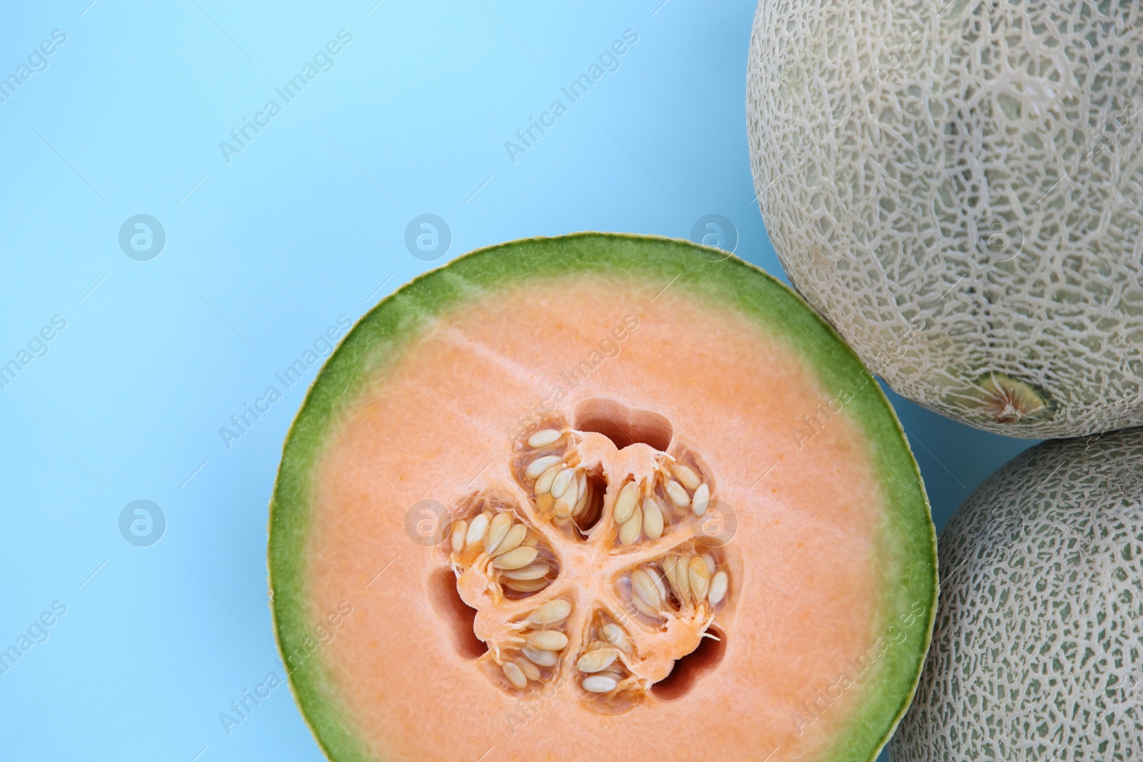 Photo of Whole and cut fresh ripe cantaloupe melons on light blue background, flat lay
