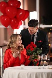 Photo of Man presenting roses to his beloved woman in restaurant at Valentine's day dinner