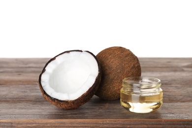 Photo of Coconuts and jar of natural organic oil on wooden table against white background