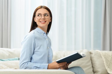 Smiling woman in stylish eyeglasses with book at home