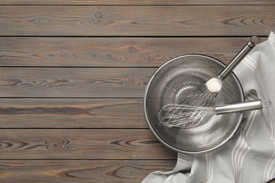 Photo of Metal whisk and spatula in colander on wooden table, flat lay with space for text. Cooking utensils