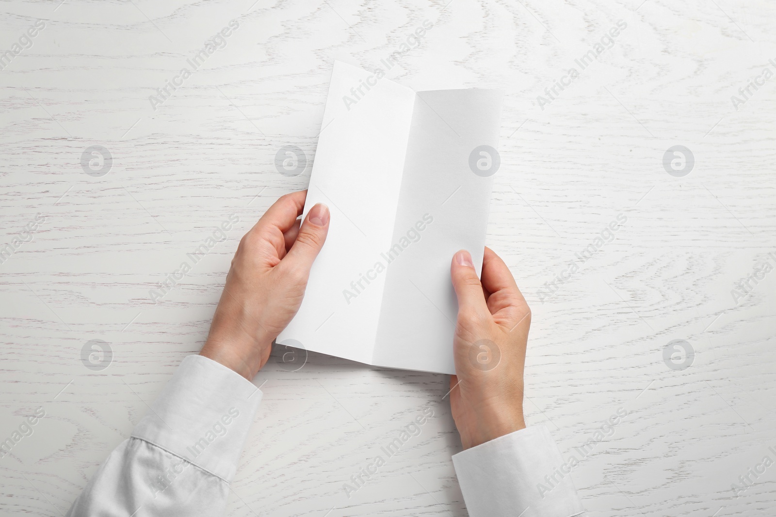 Photo of Young woman holding blank brochure at white wooden table, top view. Mock up for design