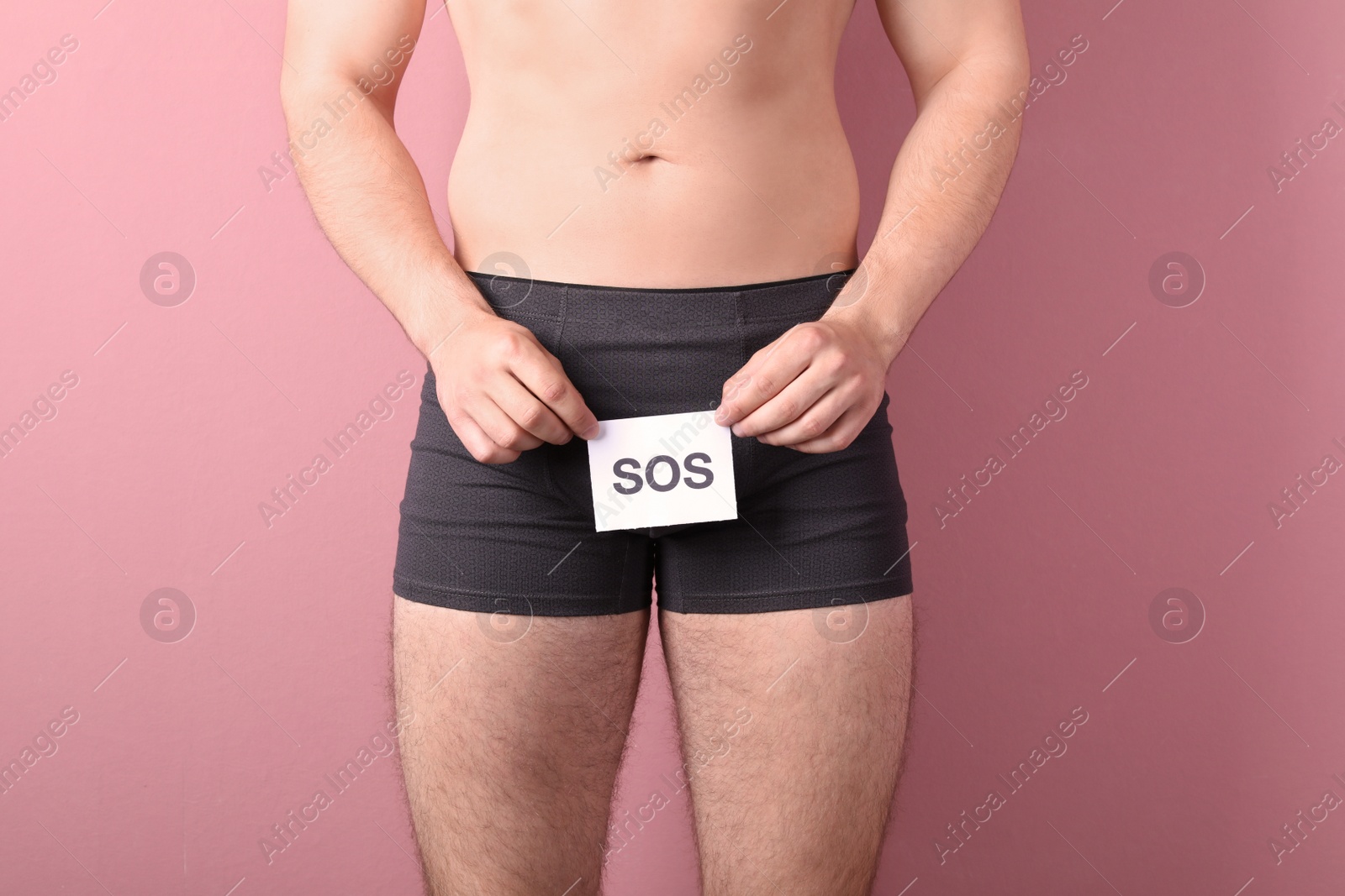 Photo of Young man with urological problems holding SOS sign on color background