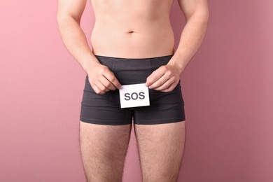 Young man with urological problems holding SOS sign on color background