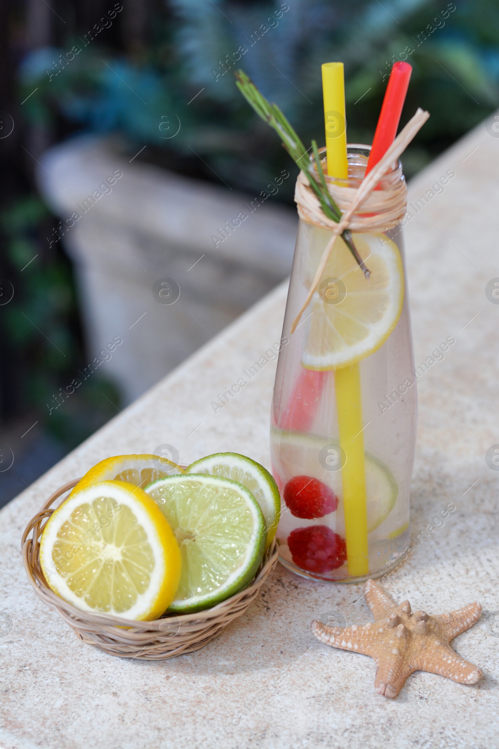 Photo of Refreshing tasty lemonade served in glass bottle and citrus fruits on beige table
