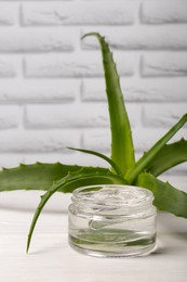 Photo of Jar of cosmetic gel and aloe vera leaves on white wooden table