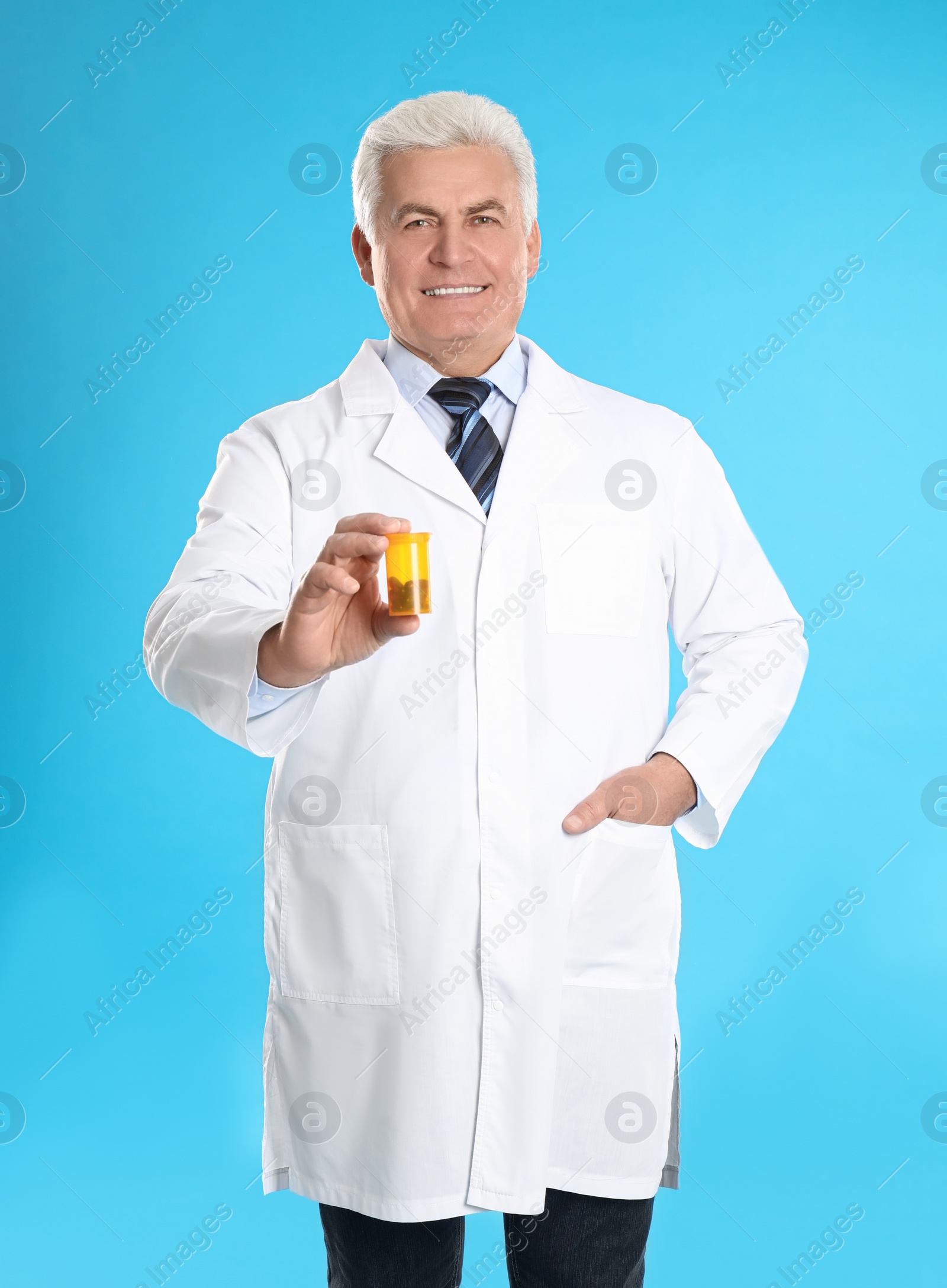 Photo of Senior pharmacist with pills on light blue background