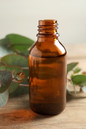 Bottle of eucalyptus essential oil and leaves on wooden table