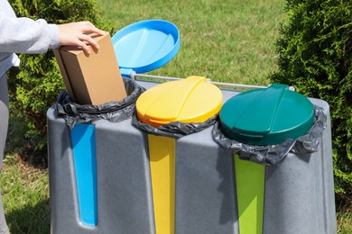 Woman throwing cardboard box in bin outdoors, closeup. Recycling concept