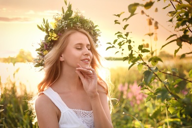 Young woman wearing wreath made of beautiful flowers outdoors on sunny day