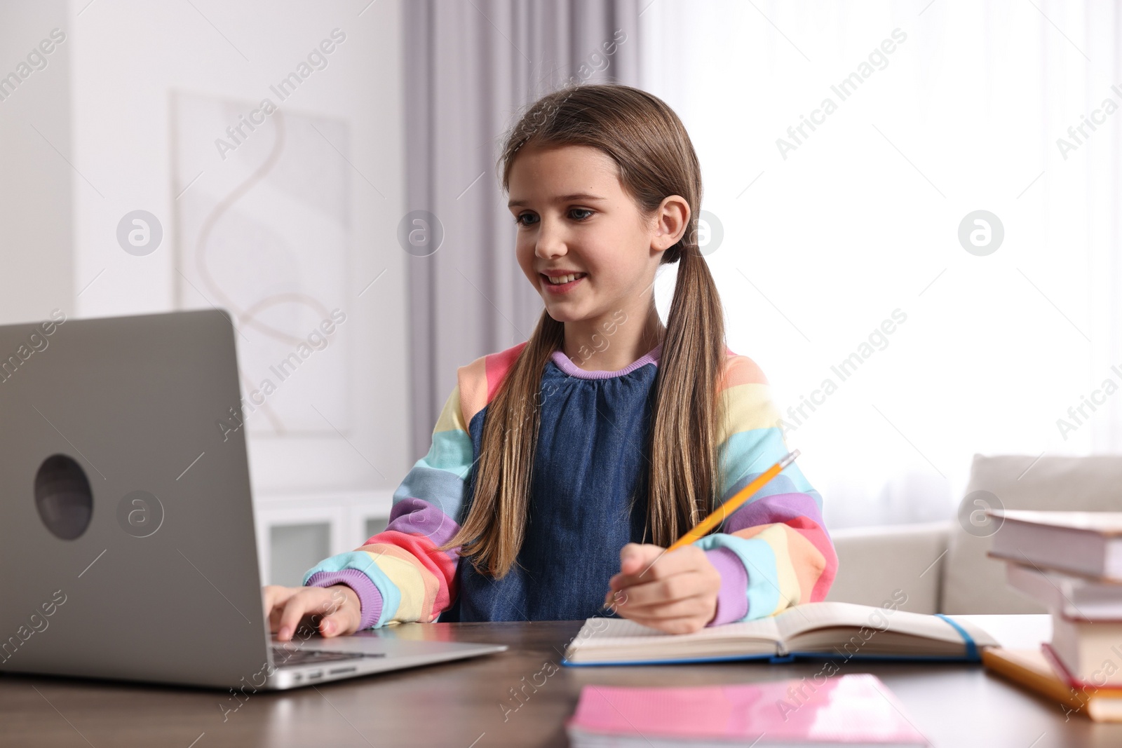 Photo of E-learning. Cute girl taking notes during online lesson at table indoors