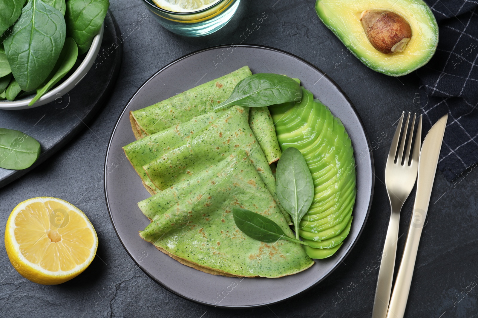 Photo of Delicious spinach crepes with avocado served on black table, flat lay