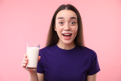 Photo of Happy woman with milk mustache holding glass of tasty dairy drink on pink background