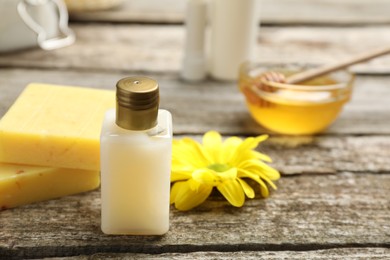 Photo of Bottle of cosmetic product and natural beeswax on wooden table, closeup