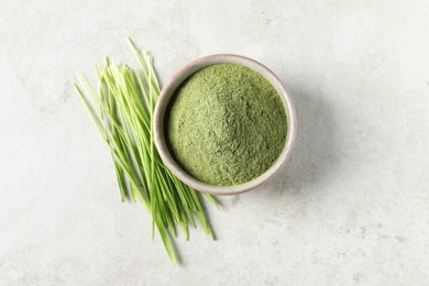 Photo of Wheat grass powder in bowl and fresh sprouts on light table, flat lay