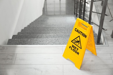 Safety sign with phrase Caution wet floor near stairs