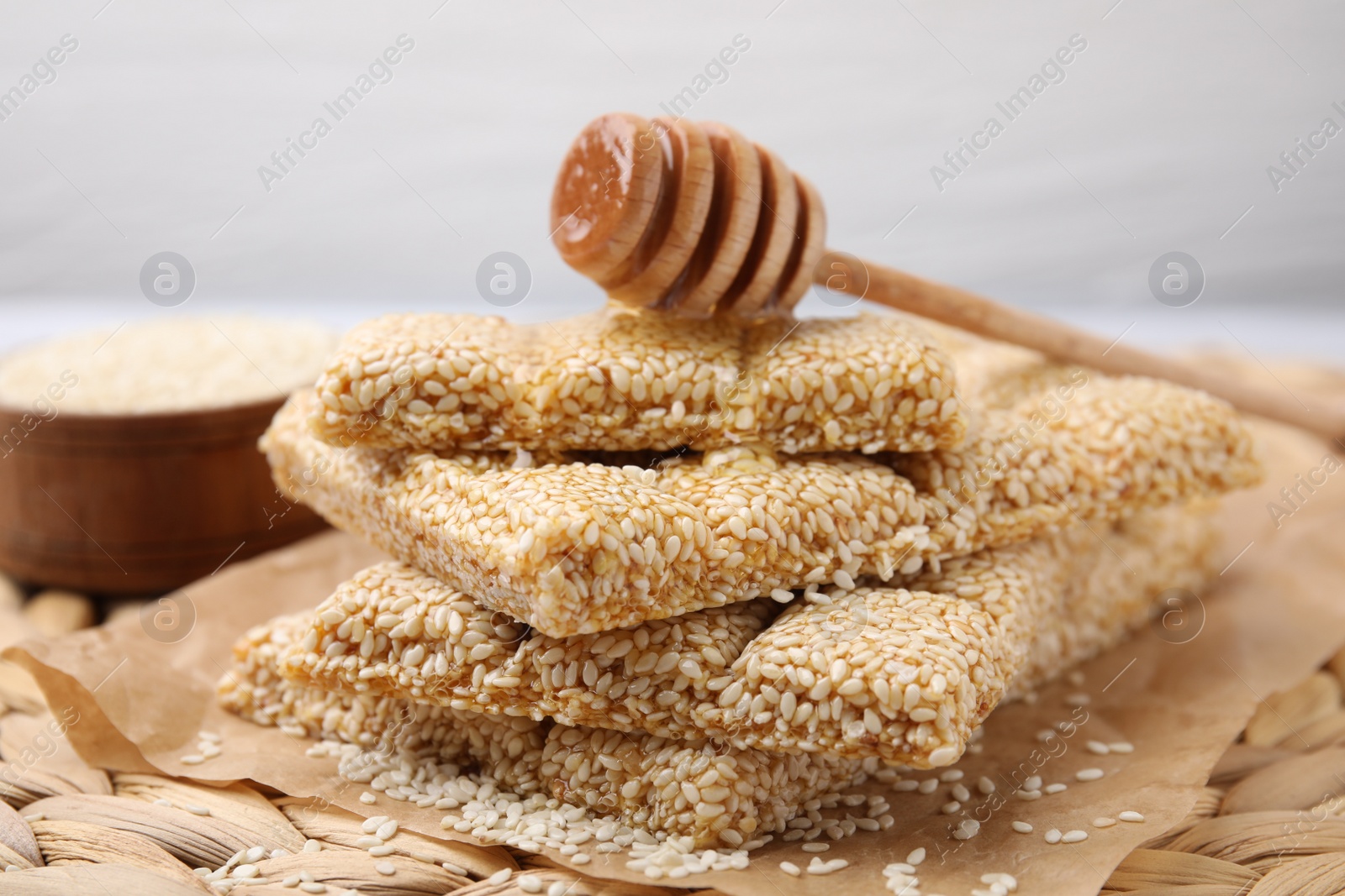 Photo of Delicious sesame kozinaki bars and wooden dipper on wicker mat, closeup