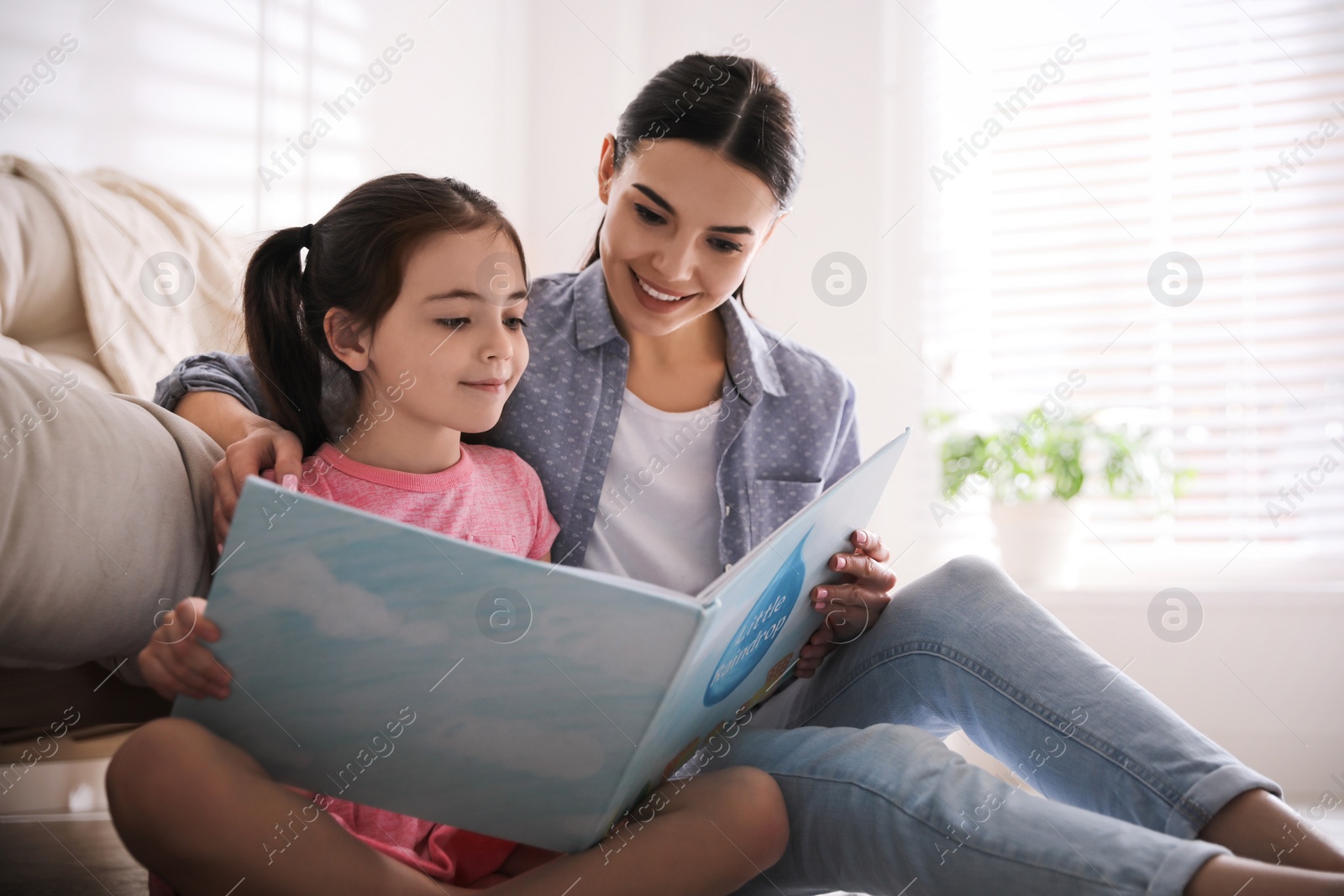 Photo of Little girl with mother reading fairy tale in living room