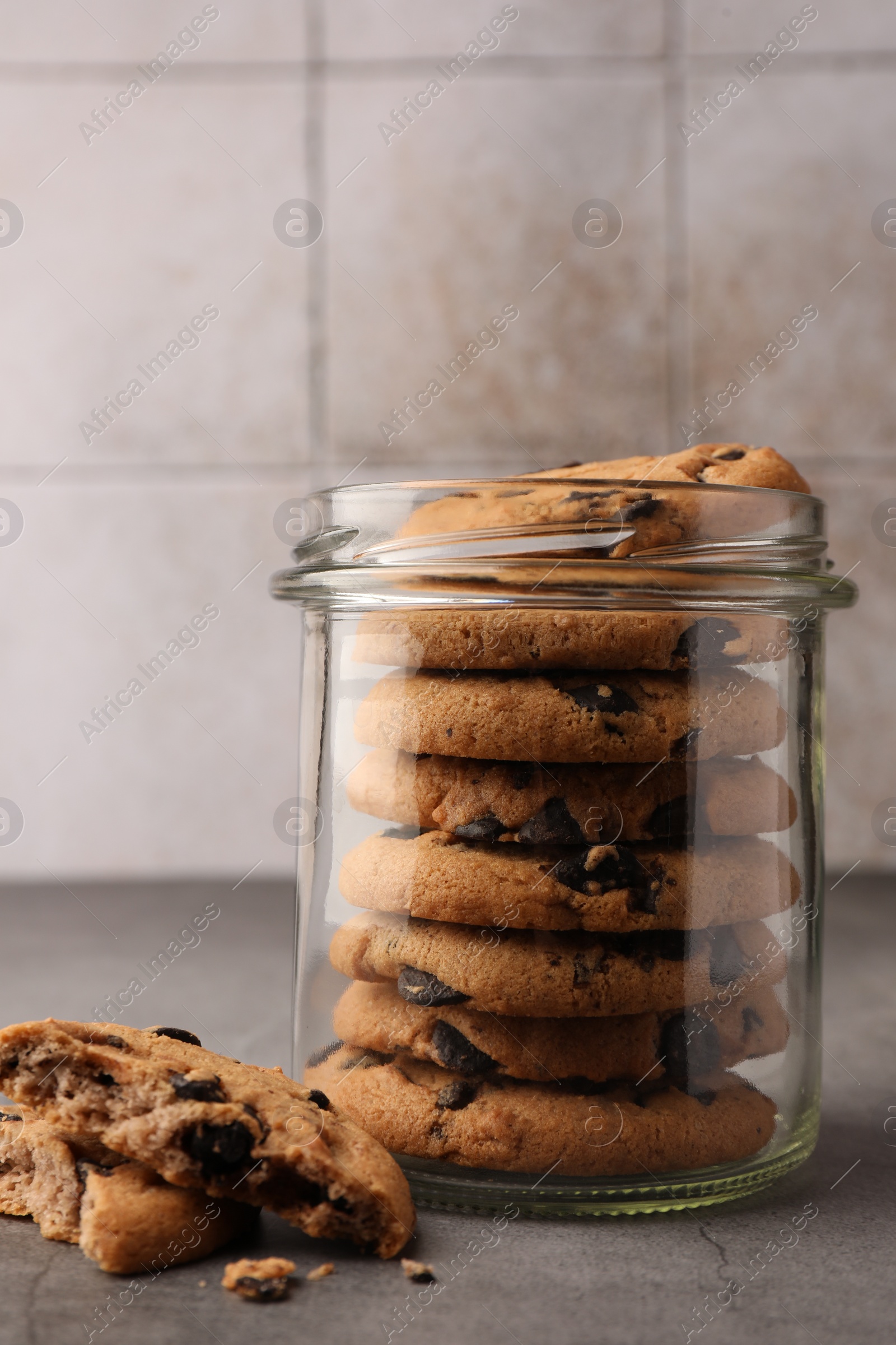 Photo of Glass jar with delicious chocolate chip cookies on grey table