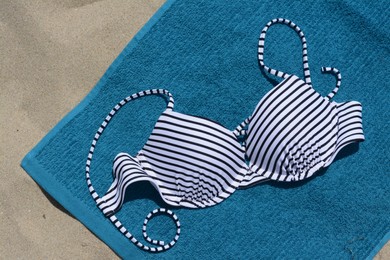 Photo of Blue beach towel and swimsuit on sand, top view