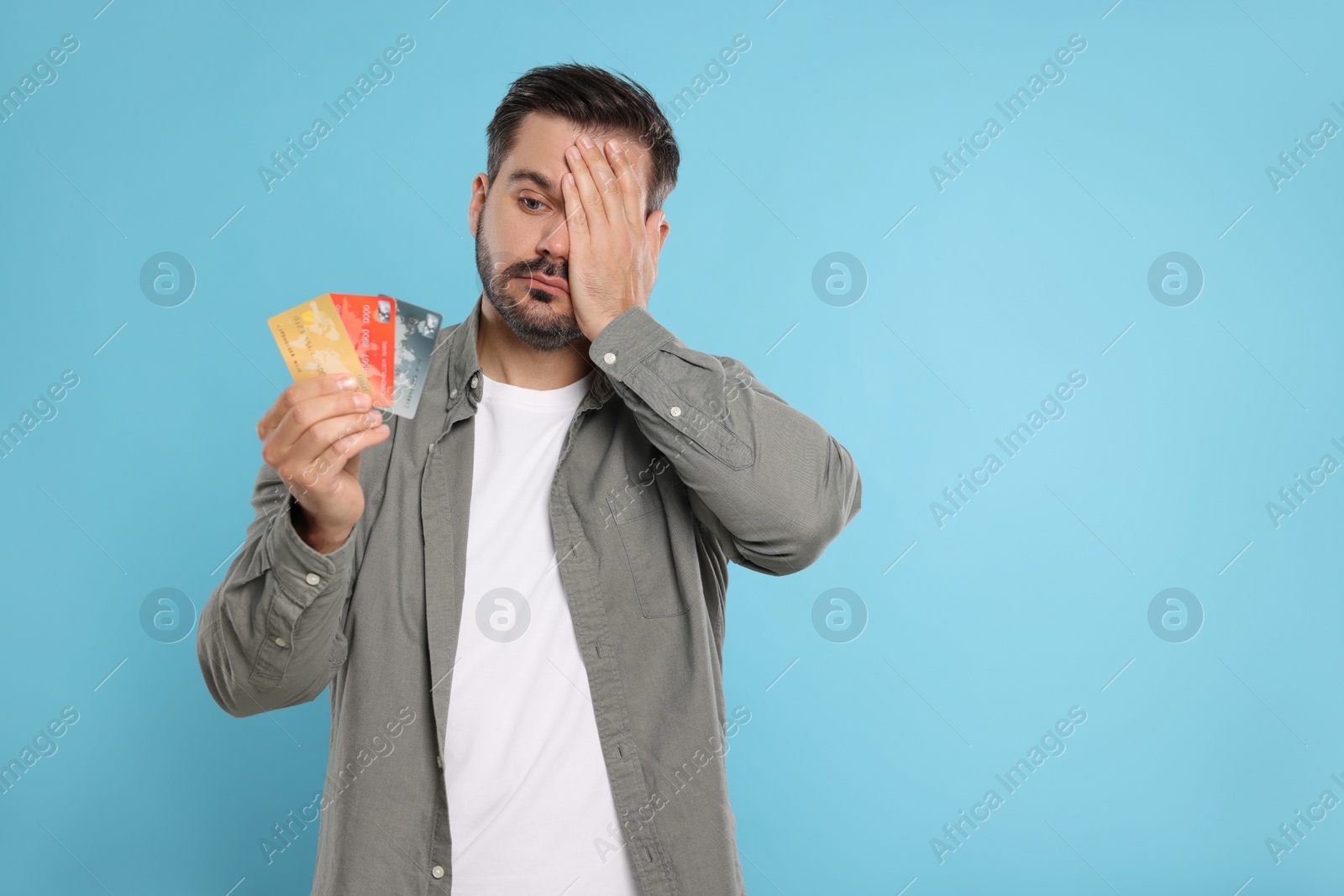 Photo of Confused man with credit cards on light blue background, space for text. Debt problem