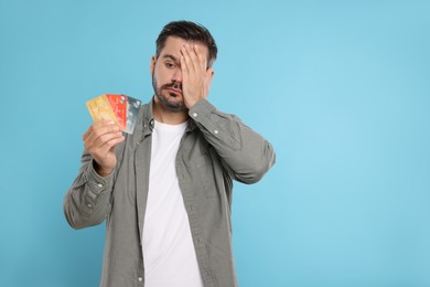 Photo of Confused man with credit cards on light blue background, space for text. Debt problem