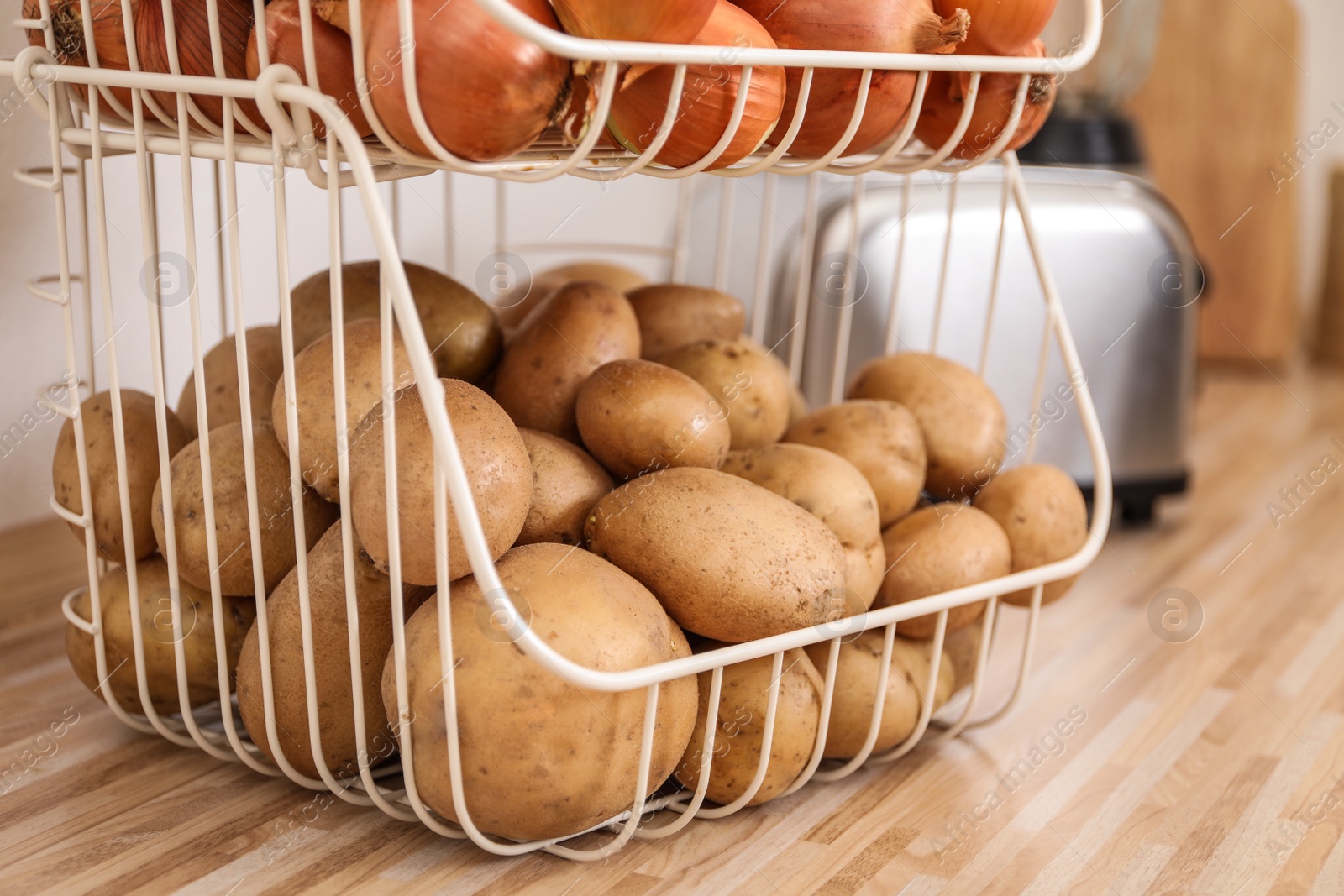 Photo of Container with potatoes and onions on wooden kitchen counter. Orderly storage