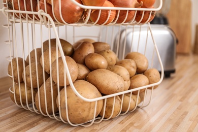 Photo of Container with potatoes and onions on wooden kitchen counter. Orderly storage