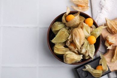 Ripe physalis fruits with calyxes on white tiled table, flat lay. Space for text