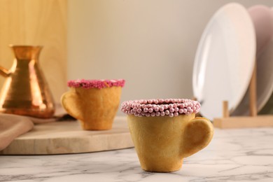 Photo of Delicious edible biscuit cup decorated with sprinkles on white marble table, space for text