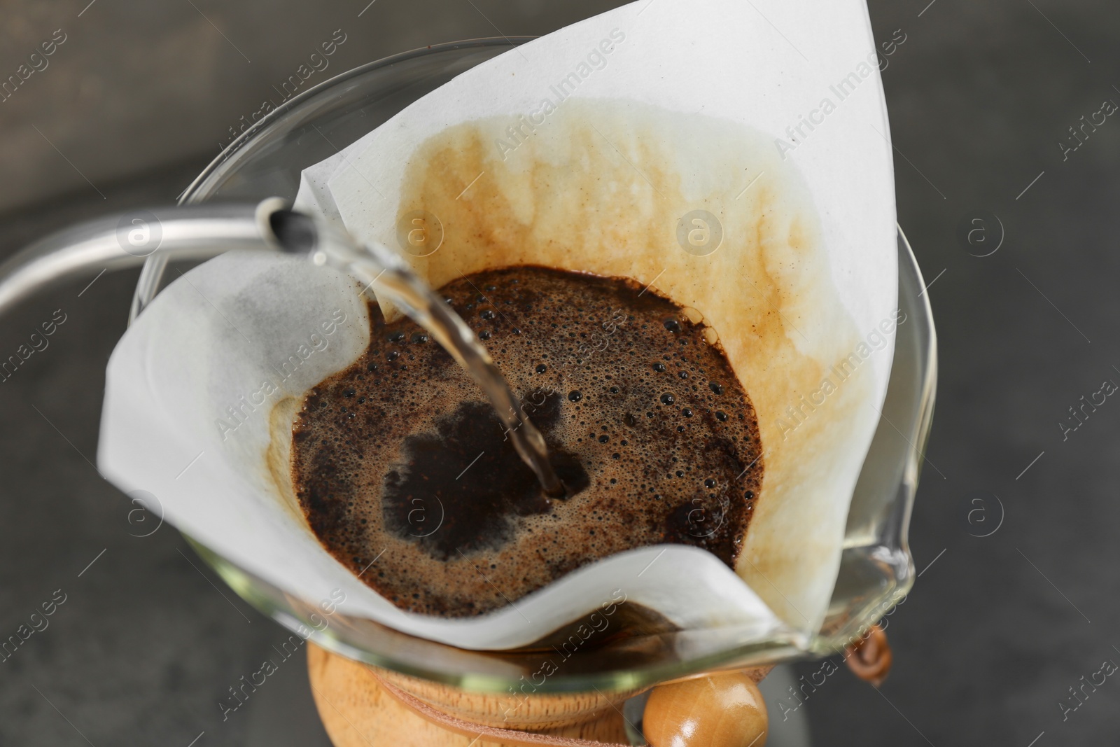 Photo of Pouring hot water into glass chemex coffeemaker with paper filter and coffee, closeup