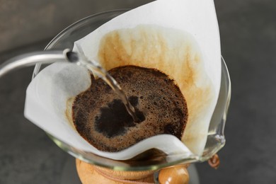 Pouring hot water into glass chemex coffeemaker with paper filter and coffee, closeup