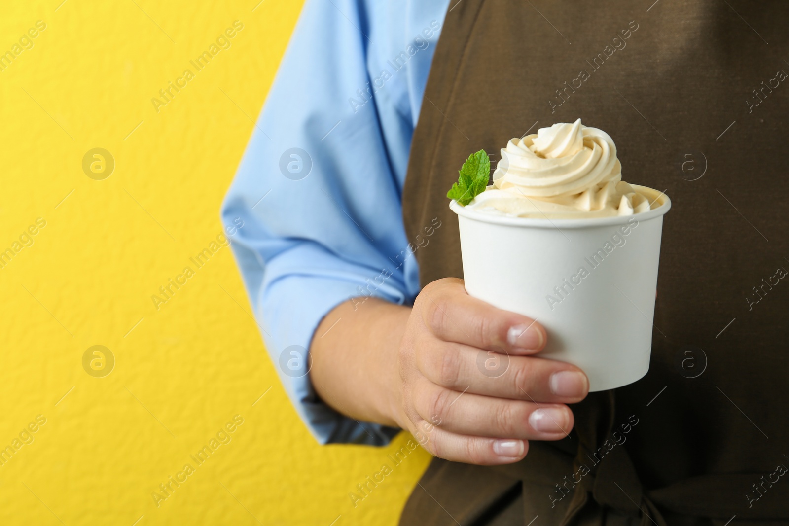 Photo of Woman holding cup with tasty frozen yogurt on yellow background, closeup