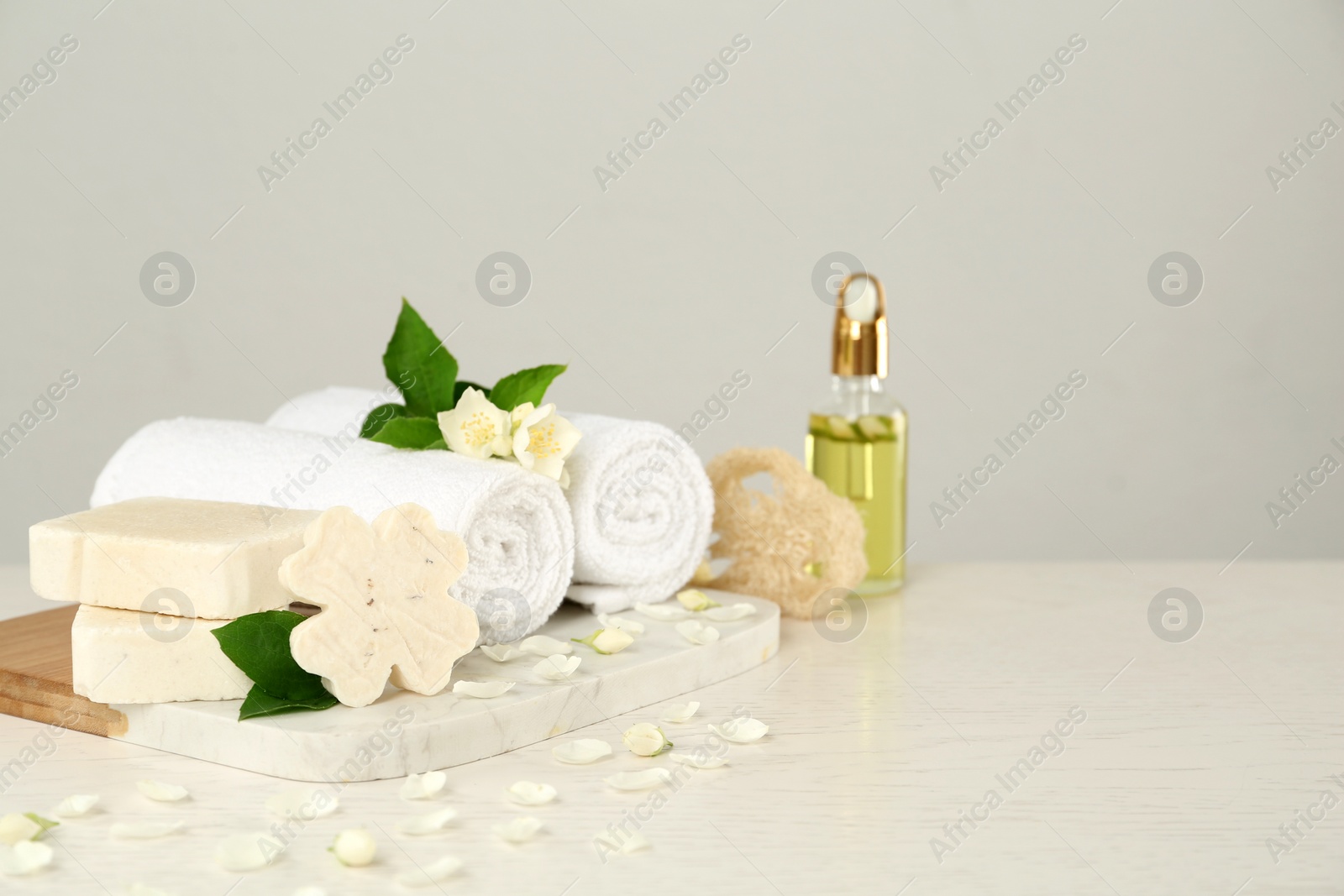 Photo of Beautiful jasmine flowers, towels and soap bars on white wooden table, space for text